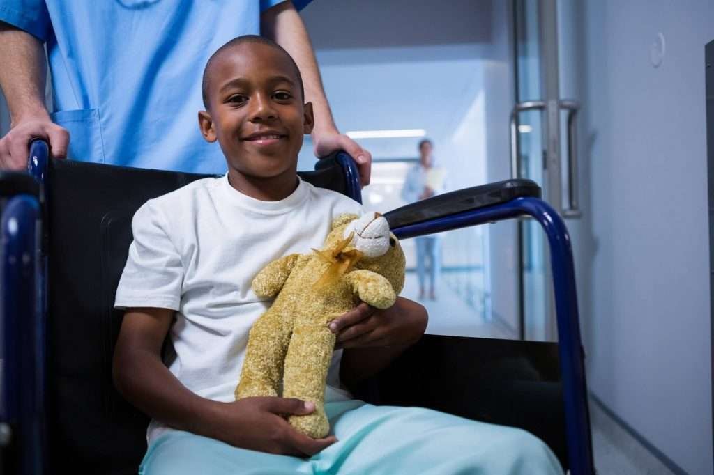 portrait-of-boy-sitting-on-wheelchair-and-holding-teddy-bear-in-corridor-1-1024×682